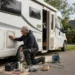 Man schuurt camper op straat in woonwijk met gereedschap en materialen rondom