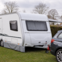 Witte toercaravan naast een auto op een Nederlandse camping of stalling, in een rustige situatie die past bij caravanverzekering.