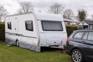 Witte toercaravan naast een auto op een Nederlandse camping of stalling, in een rustige situatie die past bij caravanverzekering.