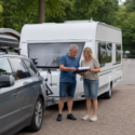 Echtpaar controleert documenten naast een aangekoppelde caravan vlak voor vertrek op vakantie.